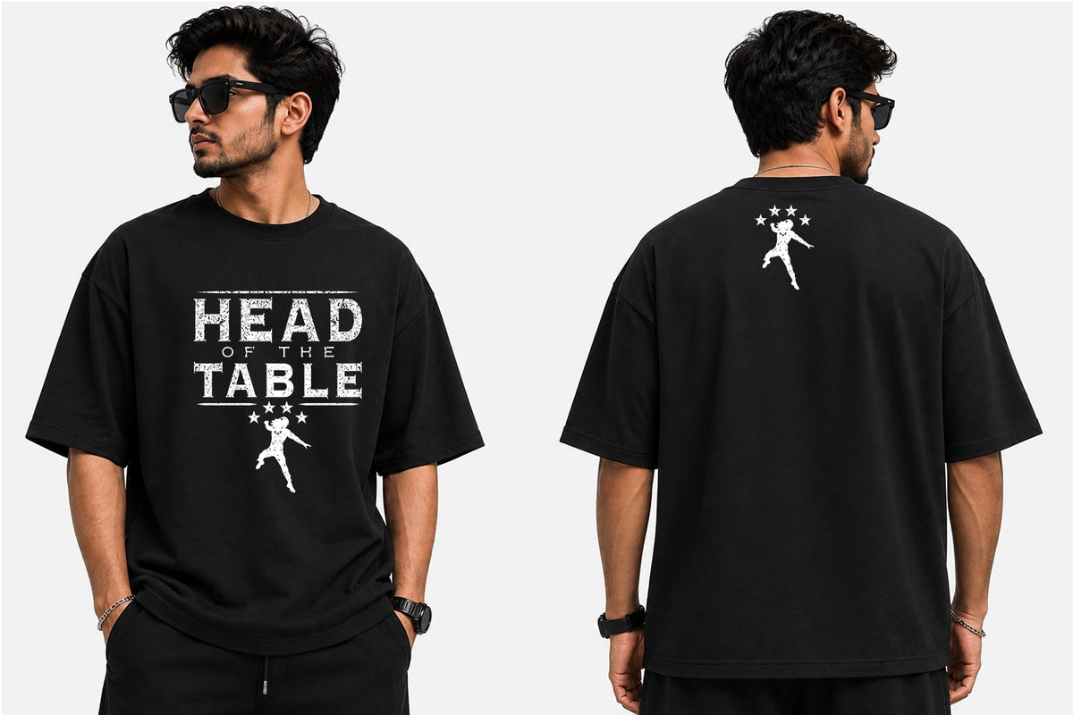 A man modeling a black graphic T-shirt shown from both front and back views against a plain light gray background. The front has large white text reading 'HEAD ON THE TABLE' with a small white graphic below, and the back has a small white graphic near the upper right shoulder area.